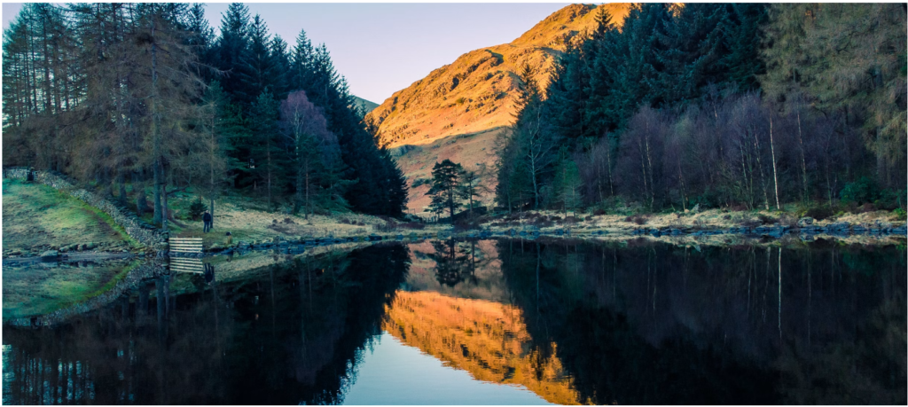 A reflective lake surrounded by trees, with a mountain in the distance.