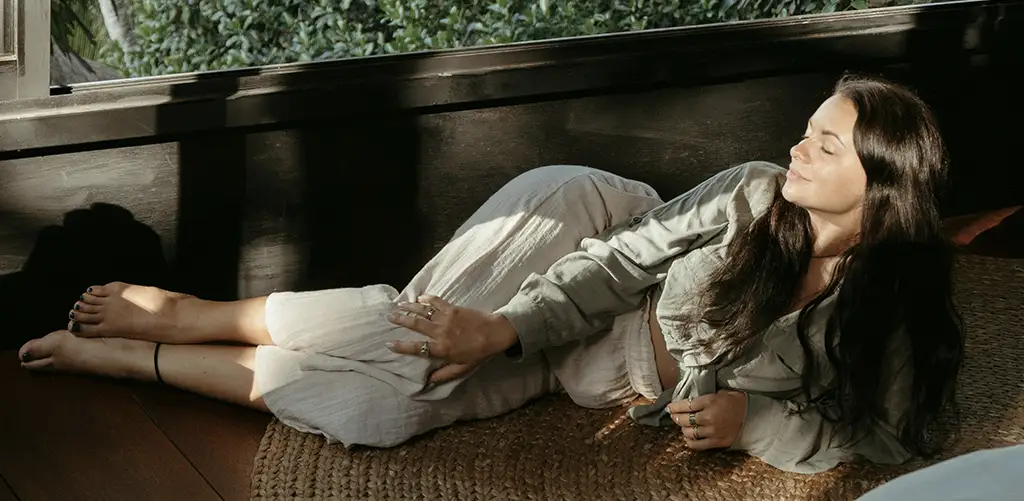 A woman relaxing on a rug, looking into the sunlight.