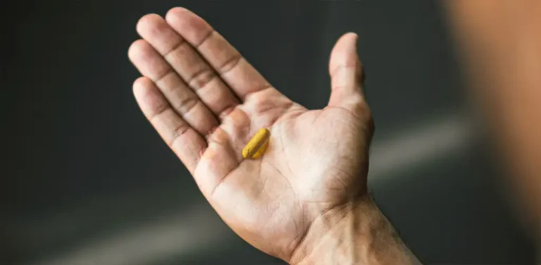 A hand with a single capsule supplement sitting on it.