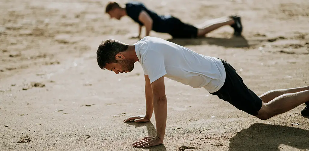 Two men doing pushups on the beach.