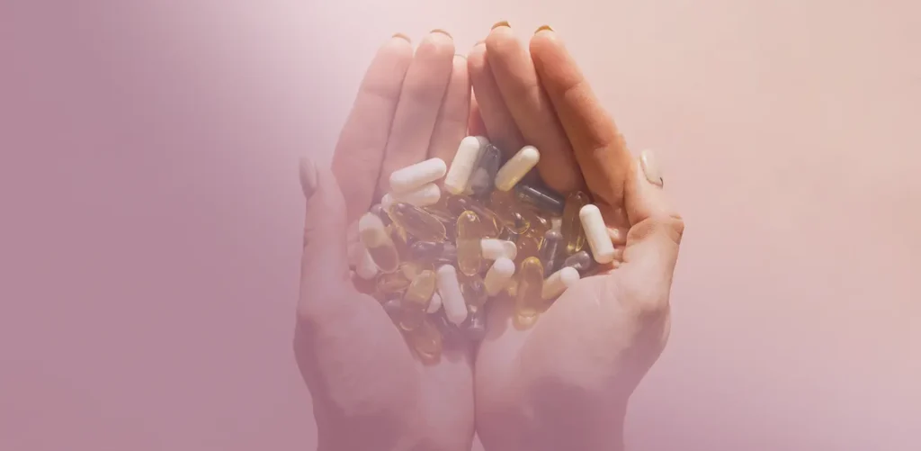 Two hands cupping a collection of pills and gel capsules.